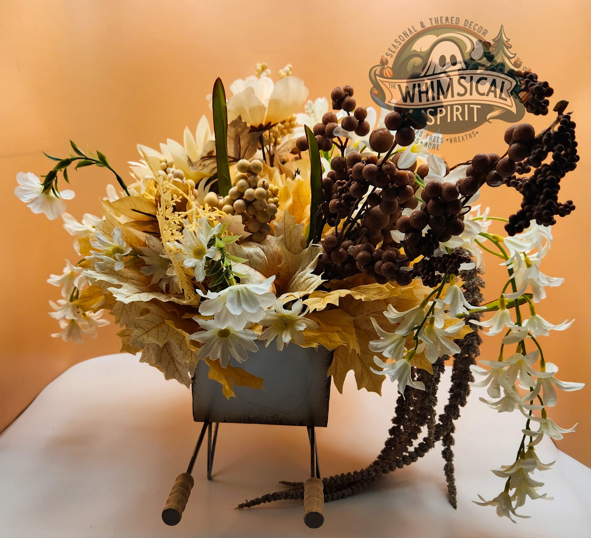Decorative flower arrangement in a small cart with 'Whimsical Spirit' branding on an orange background.
