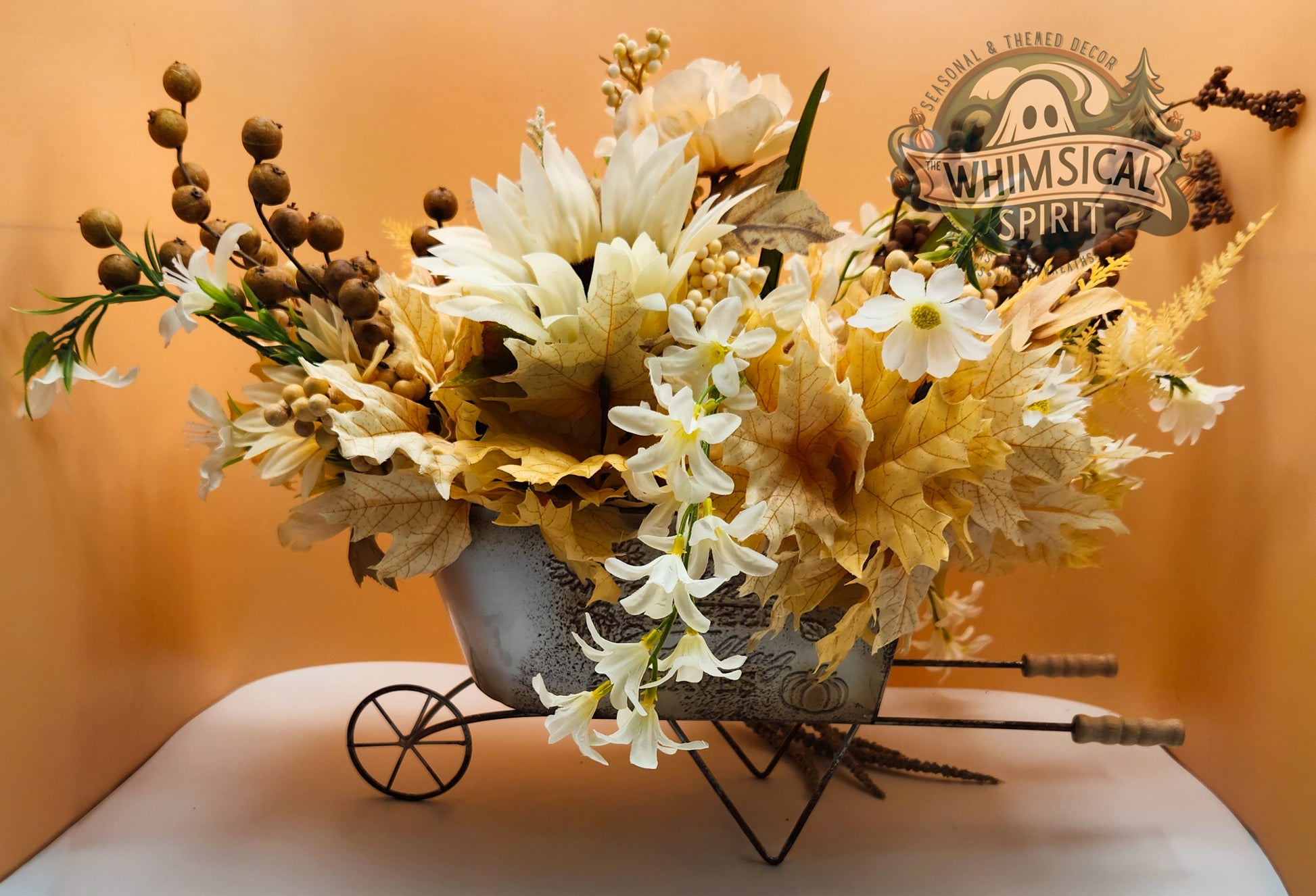 Decorative flower arrangement in a wheelbarrow with 'Whimsical Spirit' branding on an orange background.