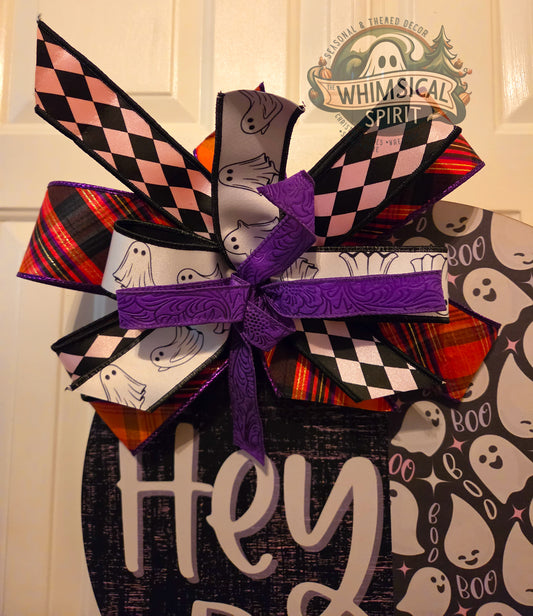 Halloween-themed decorative bow with ghost design on a wooden sign.