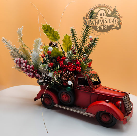 Decorative red truck with Christmas-themed floral arrangement on a white surface, branded 'Whimsical Spirit'.