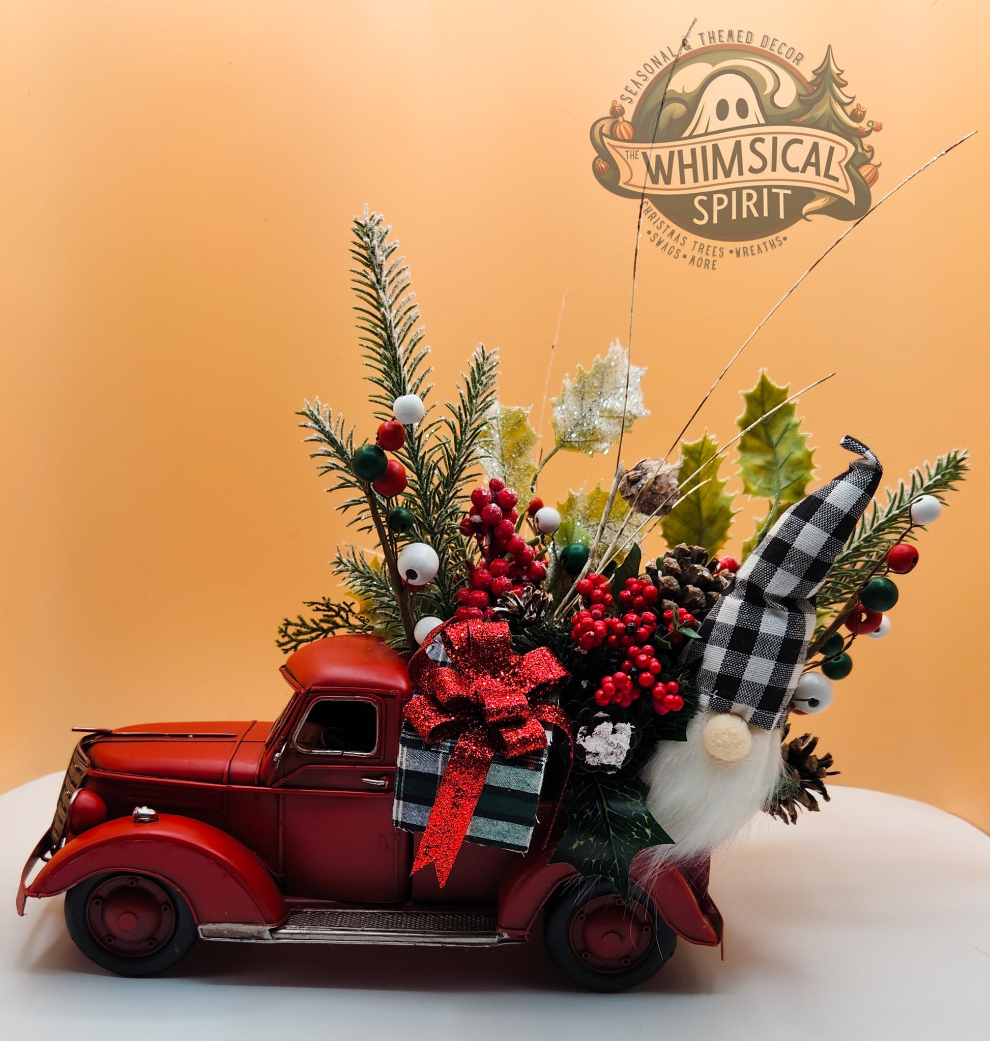 Christmas decor arrangement with red truck, festive gnome, ornaments on orange background, Whimsical Spirit logo featured