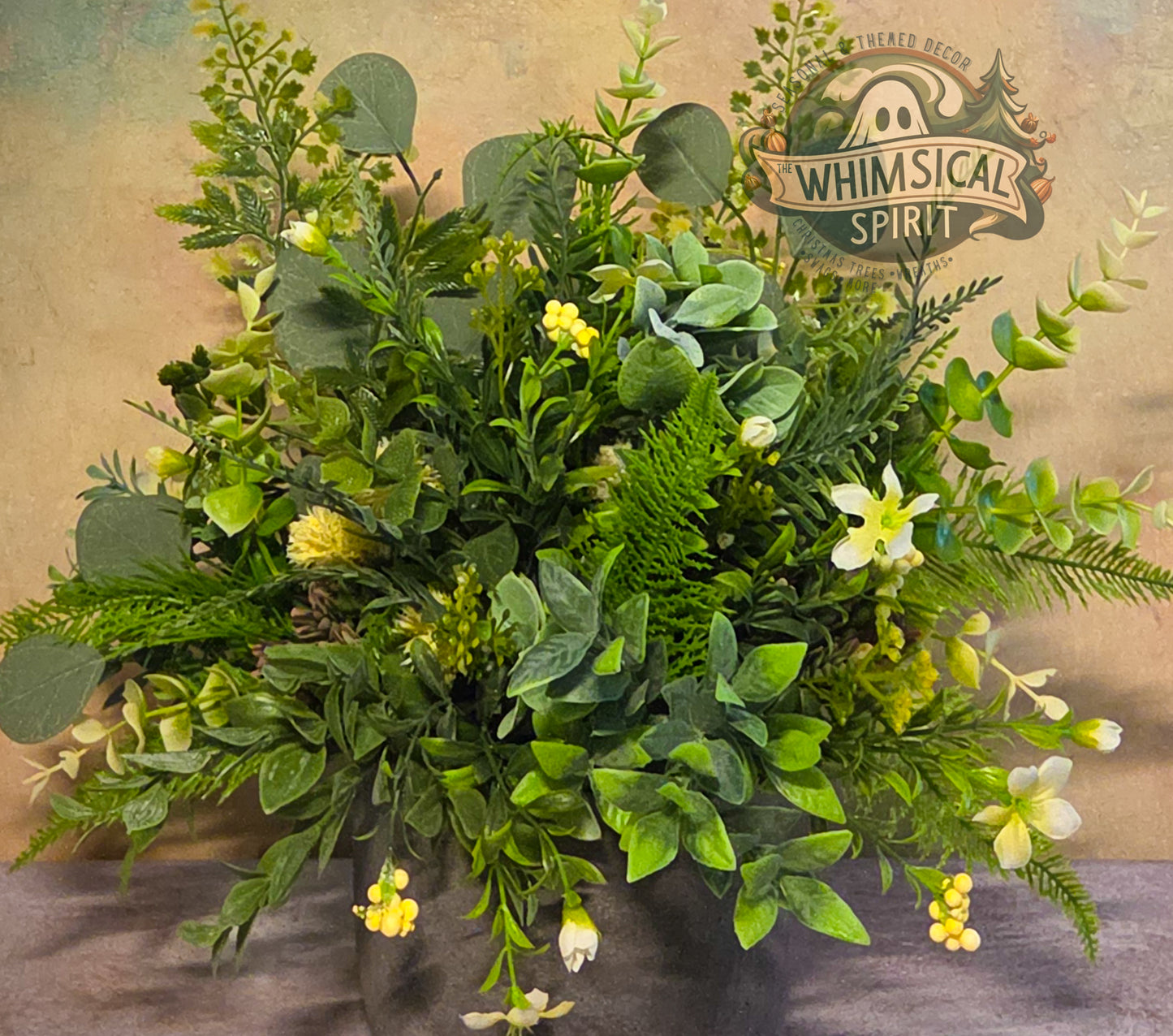Artificial greenery arrangement with yellow flowers on a textured background, featuring 'Whimsical Spirit' branding.