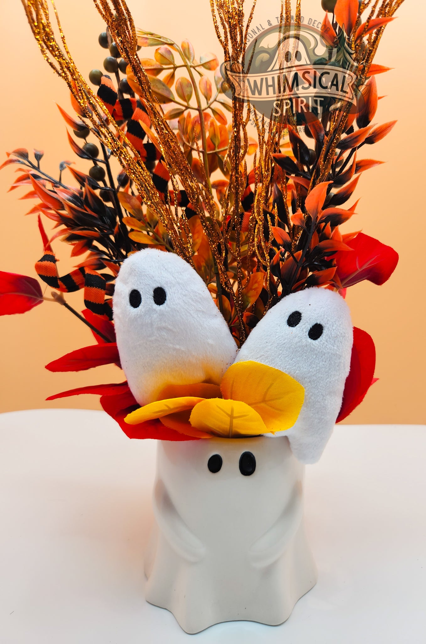 Decorative Halloween arrangement with ghost-shaped vases and a yellow leaf on a white surface.