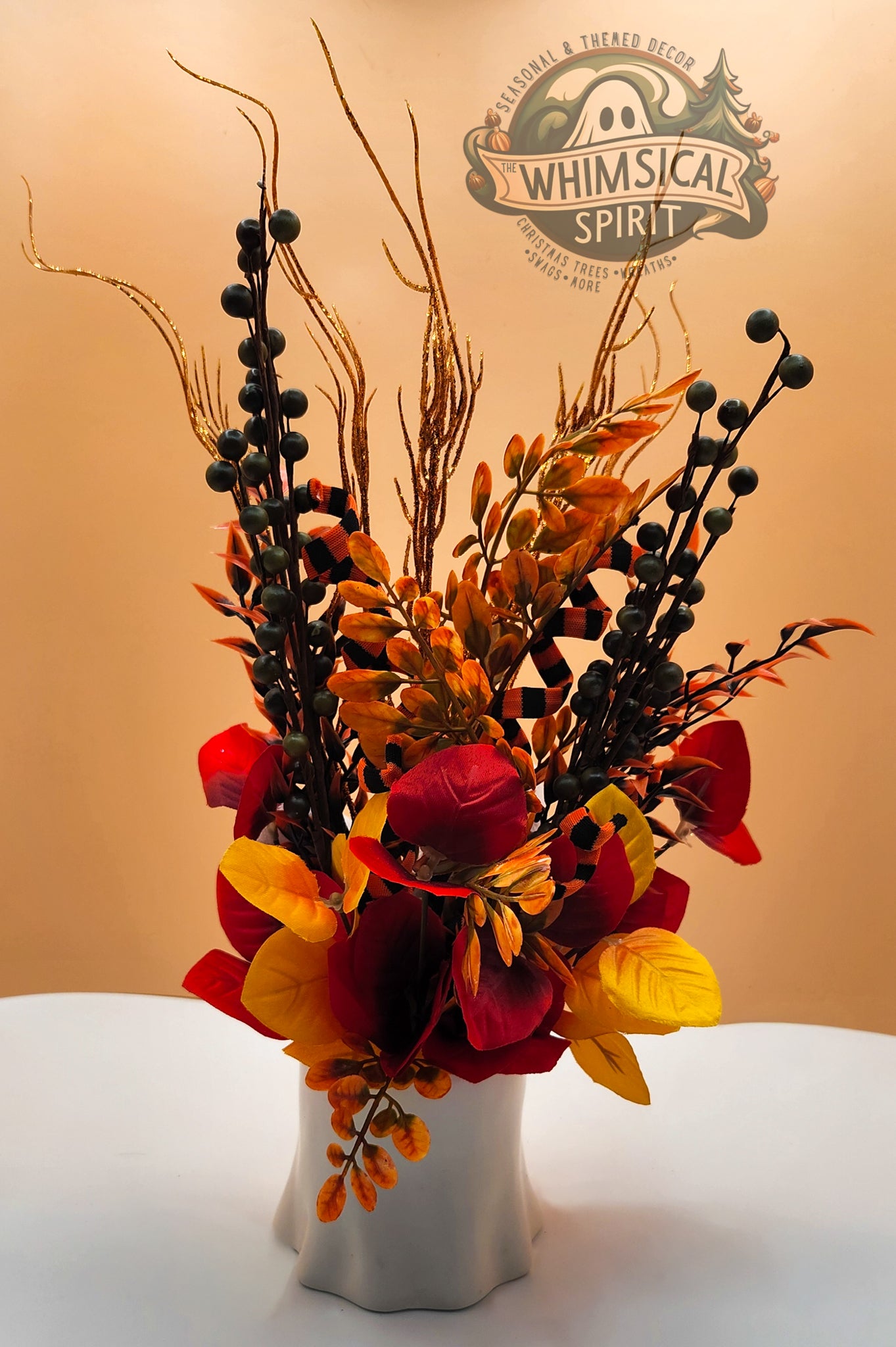 Autumnal floral arrangement with red, yellow, and black flowers in a white vase on a beige background with 'Whimsical Spirit' logo.