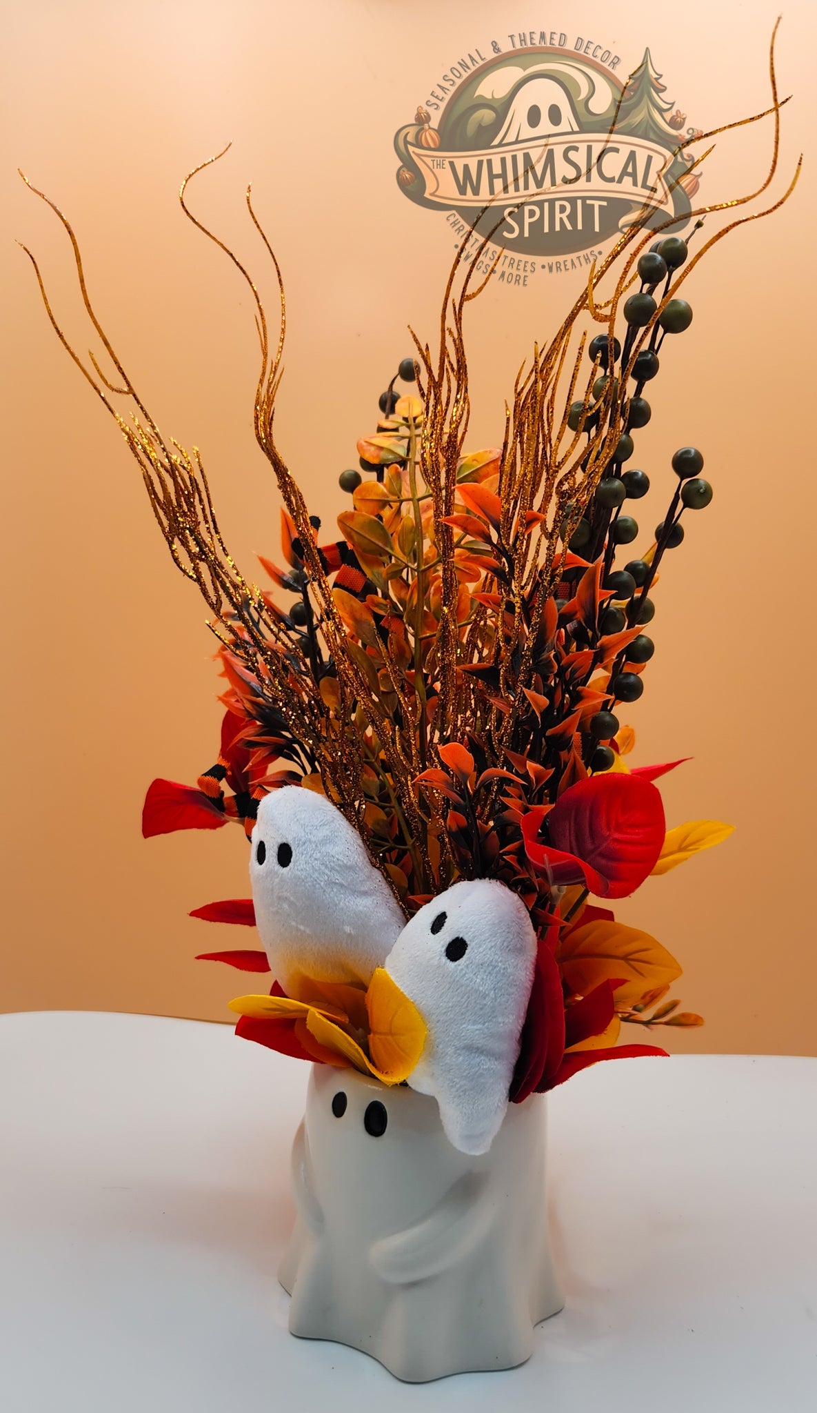 Decorative arrangement with ghost figures, autumn leaves, and branches on a white surface with a beige background.