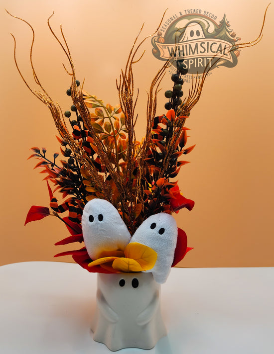 Decorative arrangement with white ghosts, red leaves, and autumnal branches on a beige background.