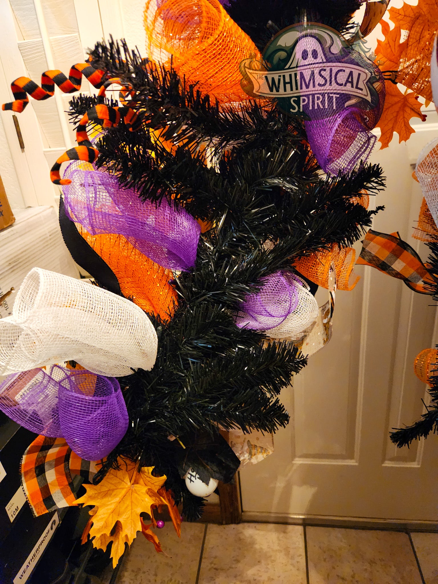 Halloween-themed wreath with black tinsel, orange and purple ribbons, and candy corn decorations on a door.