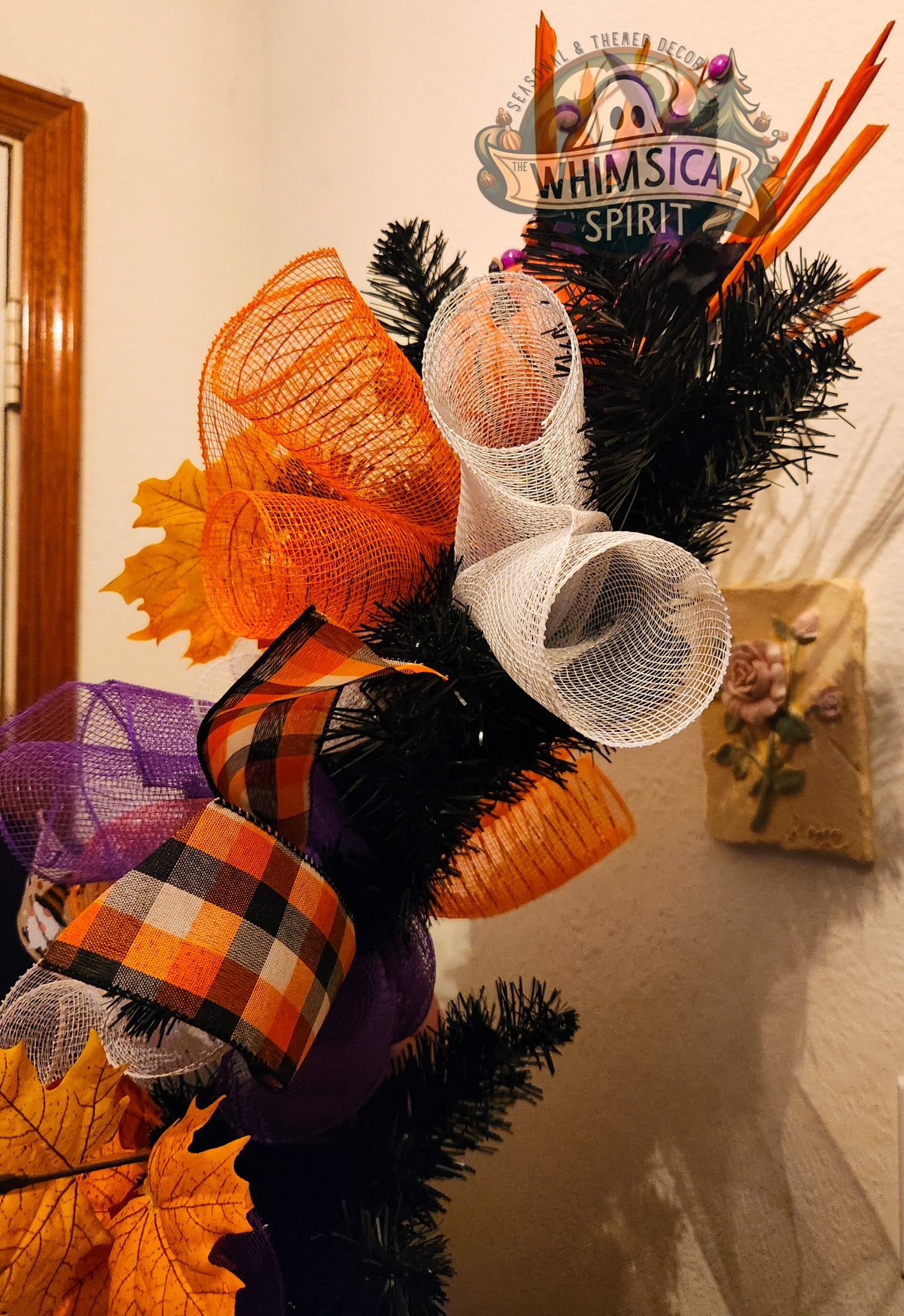 Decorative Halloween wreath with pumpkins, ribbons, and leaves on a plain background.