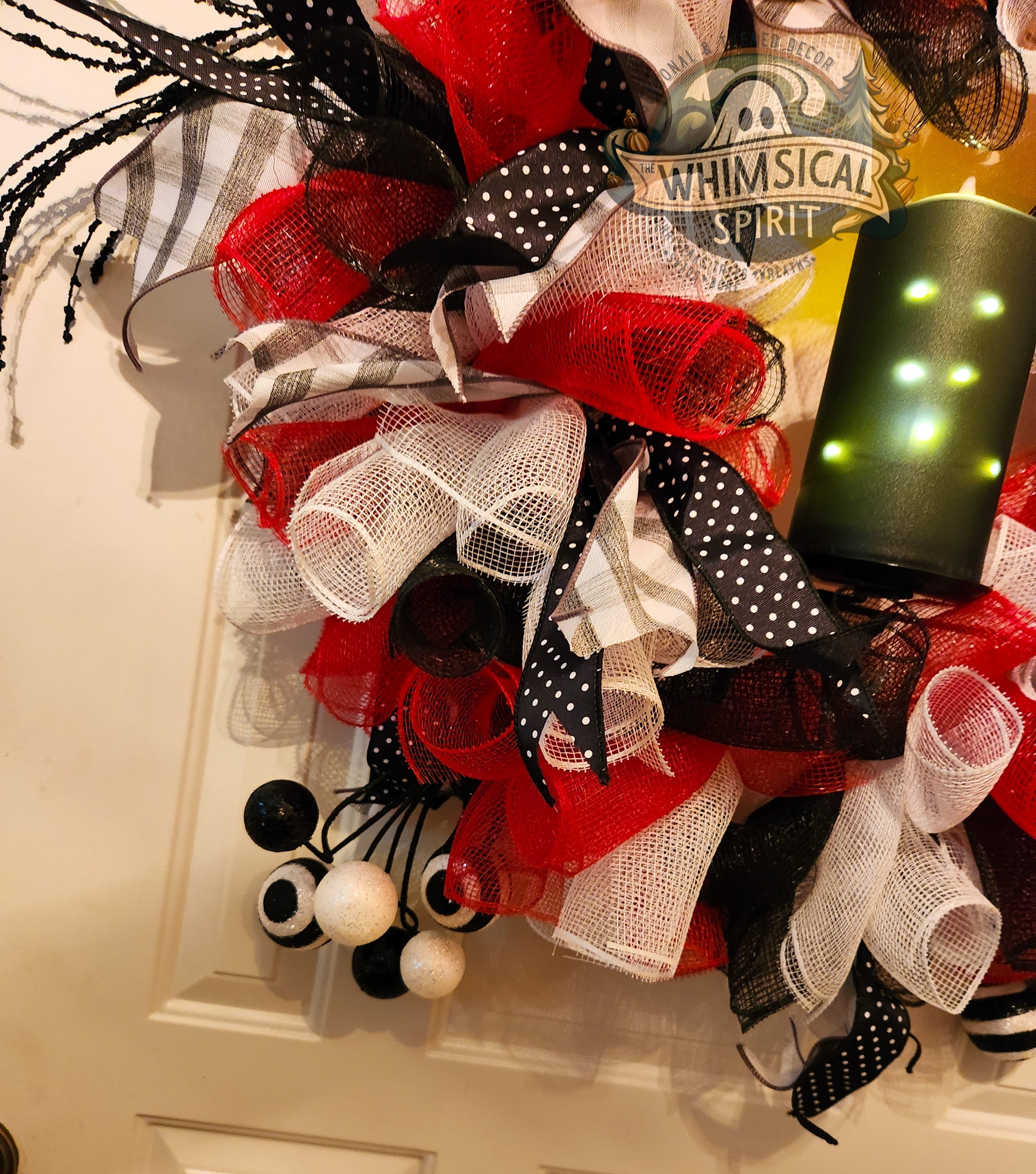 Halloween Decorative wreath with orange, white, and black ribbons on a door with 'Whimsical Spirit' sign.