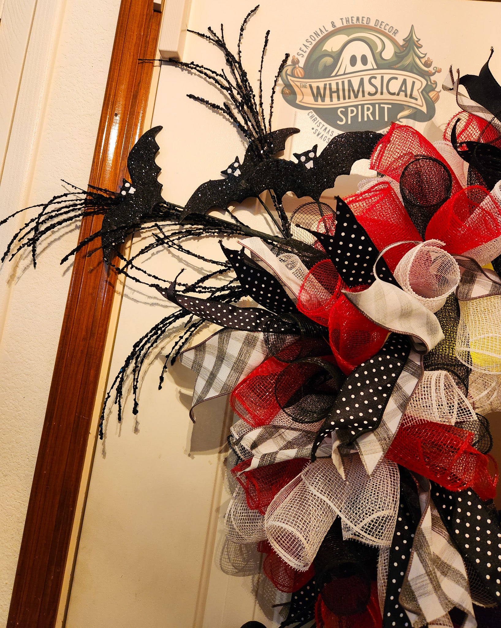 Decorative wreath with black, red, and white ribbons on a door, featuring 'Whimsical Spirit' branding.