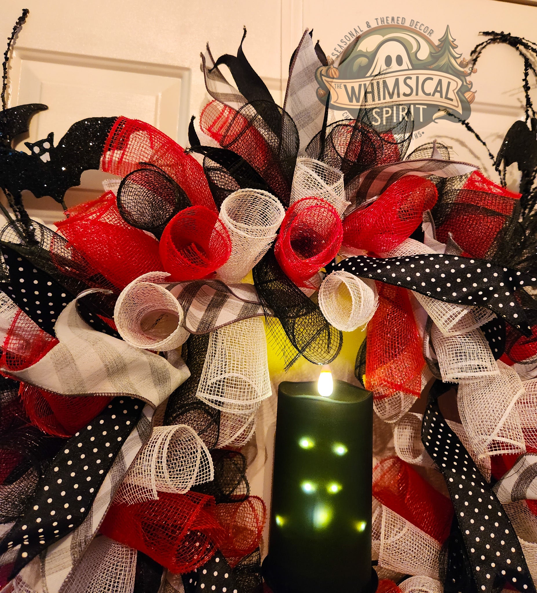 Halloween Decorative wreath with orange, white, and black ribbons and black glittered bats on a door with 'Whimsical Spirit' sign.