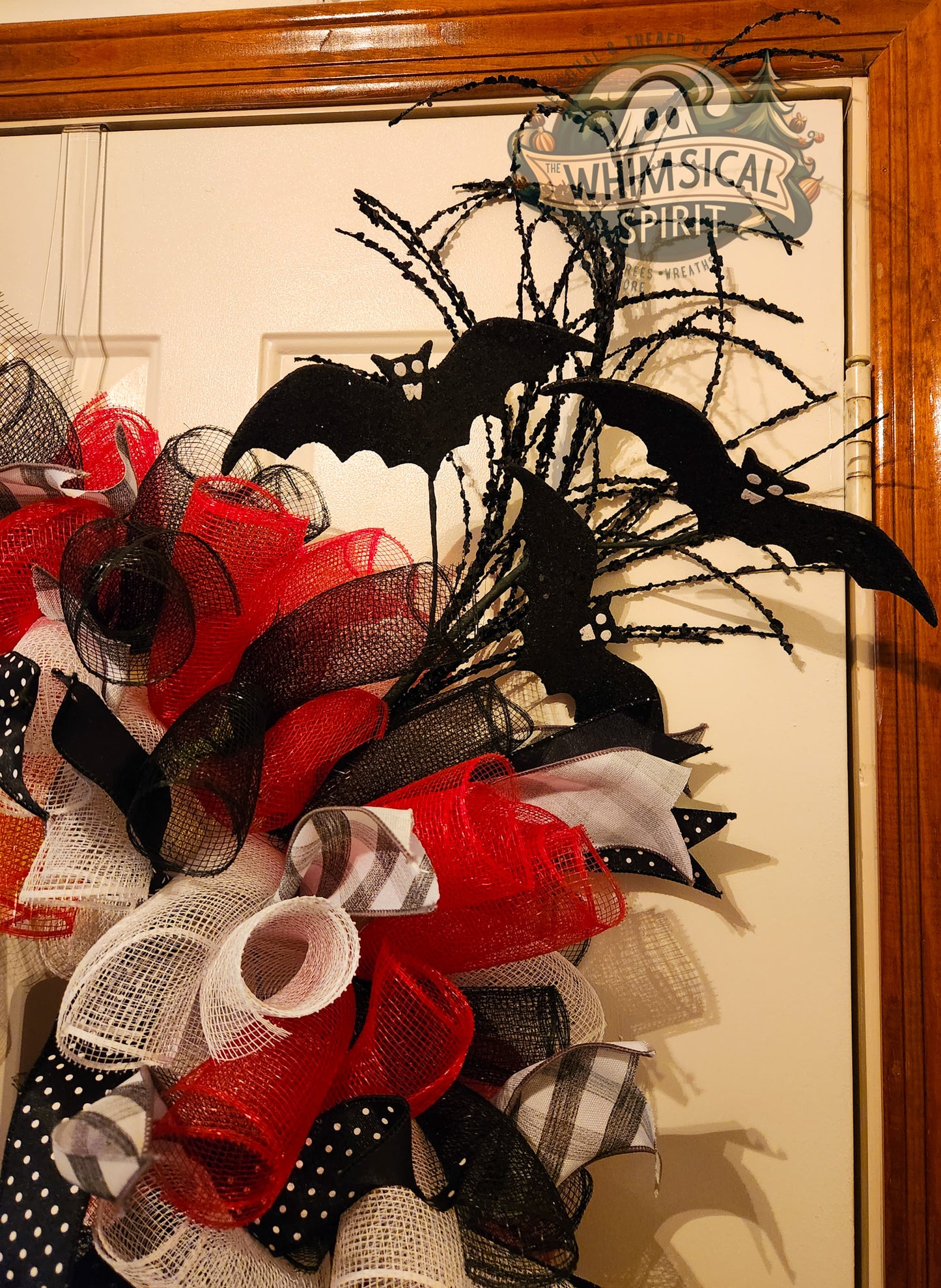 Halloween-themed decorative wreath with black bats, red ribbons, and other festive elements on a door.