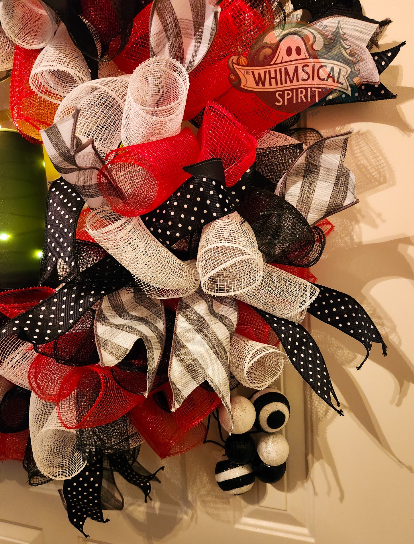 Decorative wreath with red, black, and white ribbons on a door.