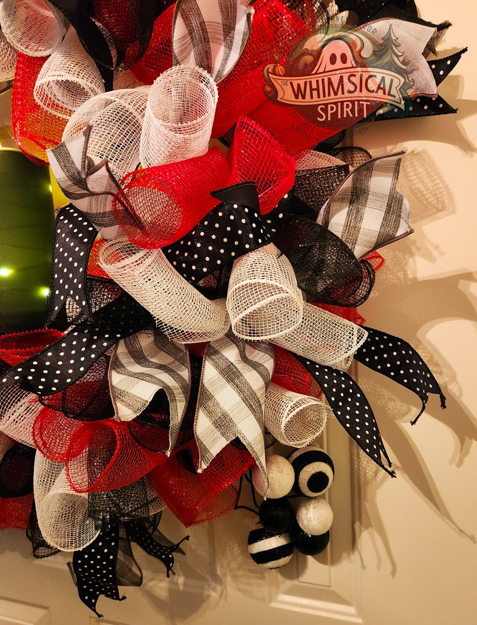 Decorative wreath with red, black, and white ribbons on a door.