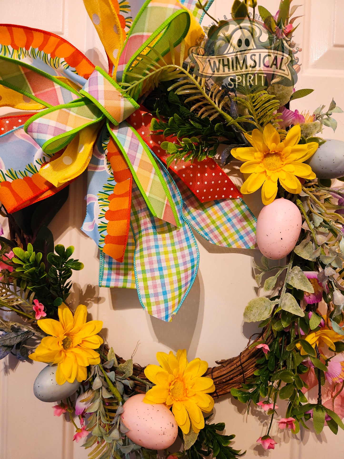 Colorful Easter wreath with flowers, ribbons, and eggs on a door.