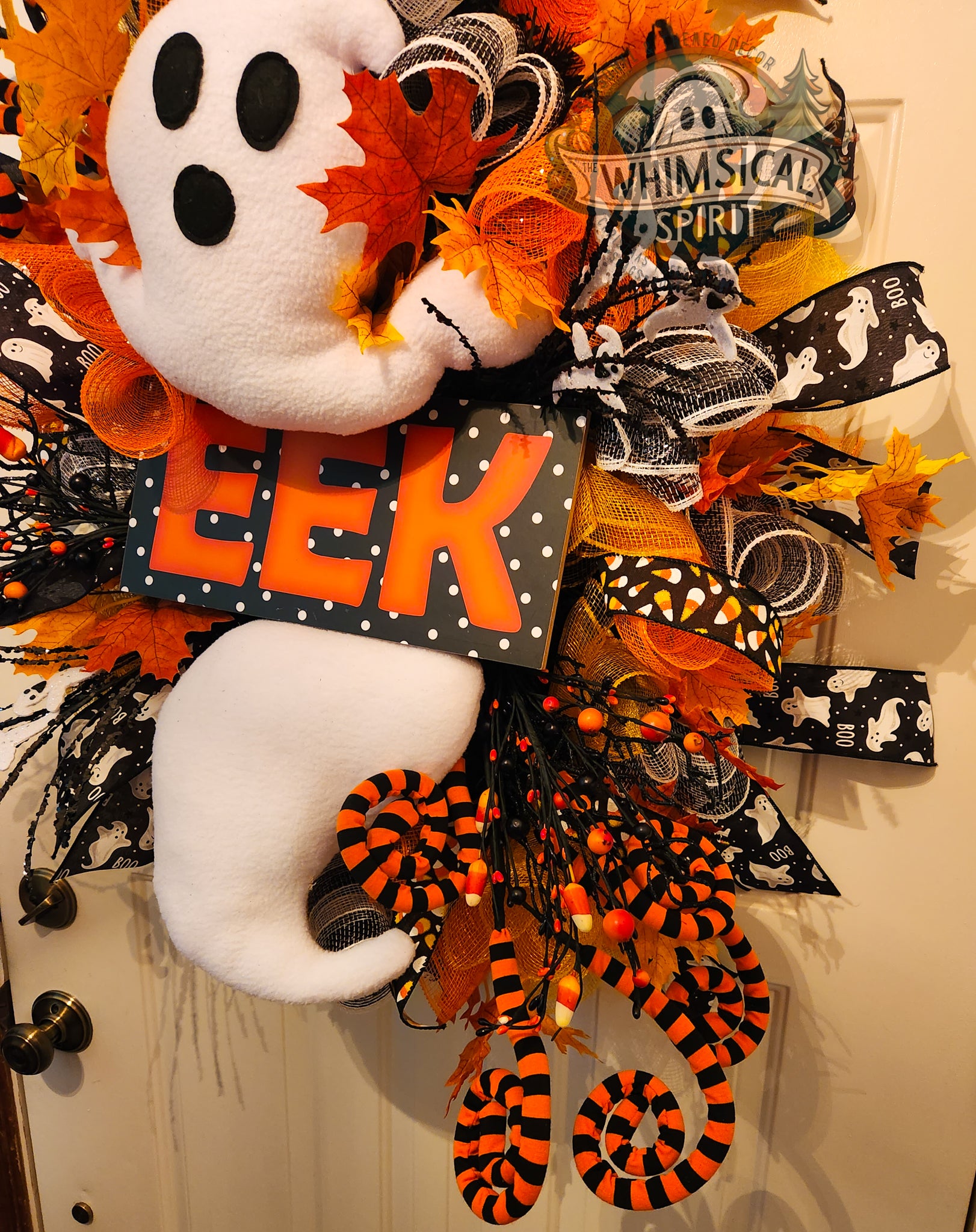 Halloween-themed wreath with ghost, snake, and 'EEK' sign on a door.