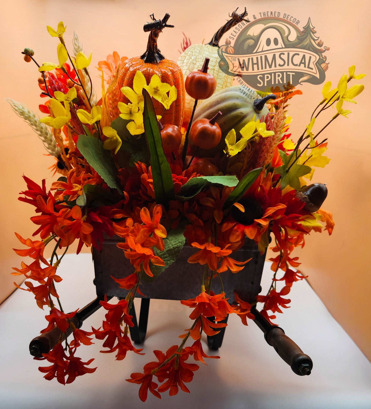 Decorative wheelbarrow with autumn-themed flowers and pumpkins, branded 'Whimsical Spirit'.