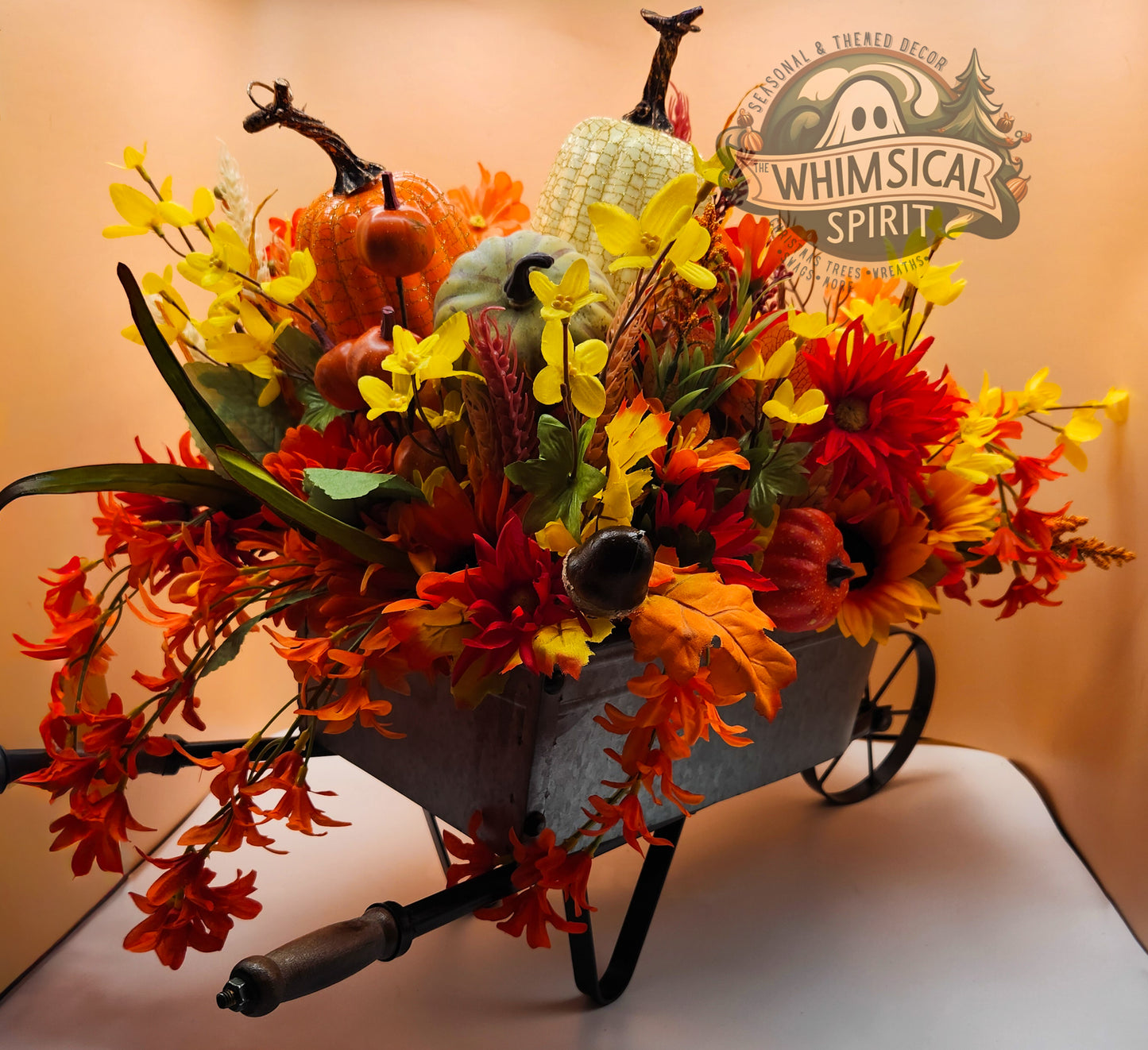Decorative wheelbarrow filled with autumn-themed flowers and pumpkins, branded 'Whimsical Spirit'.