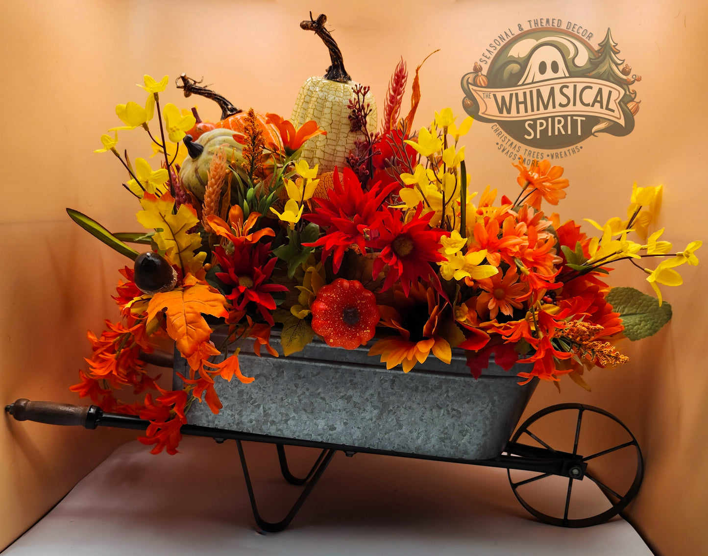 Decorative wheelbarrow with autumn-themed flowers and pumpkins, featuring 'Whimsical Spirit' branding.