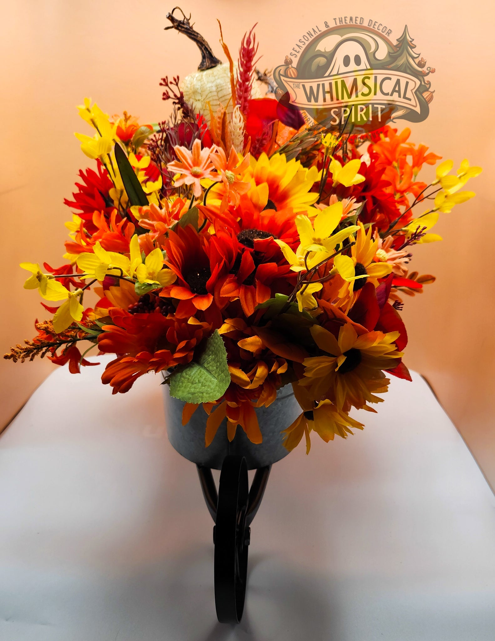 Autumn-themed floral arrangement with pumpkins on a white surface, branded 'Whimsical Spirit'.