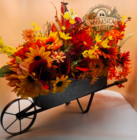 Decorative wheelbarrow filled with autumn-themed flowers on a plain background