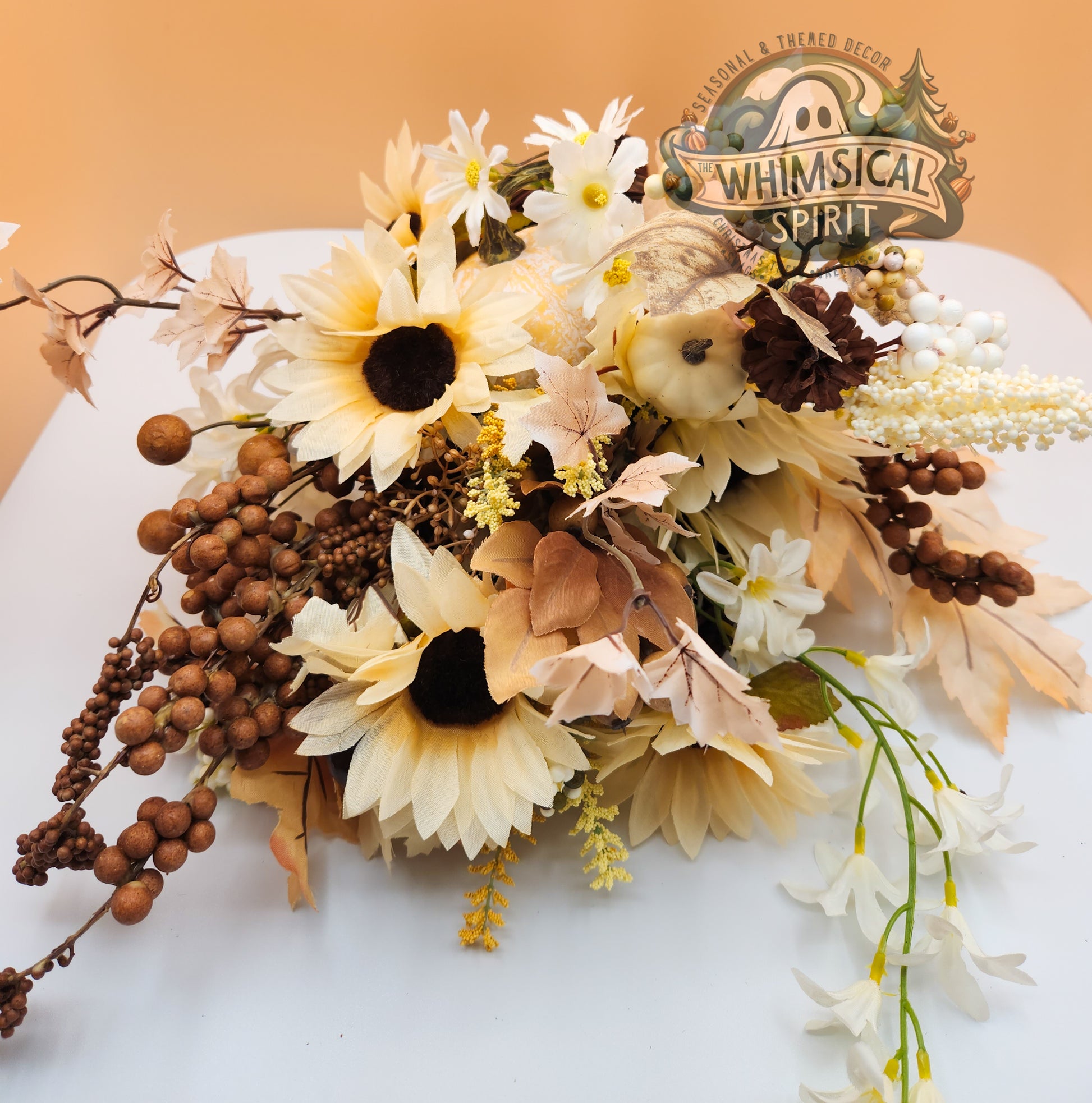 Decorative floral arrangement with sunflowers and berries on a white surface, featuring 'Whimsical Spirit' logo.