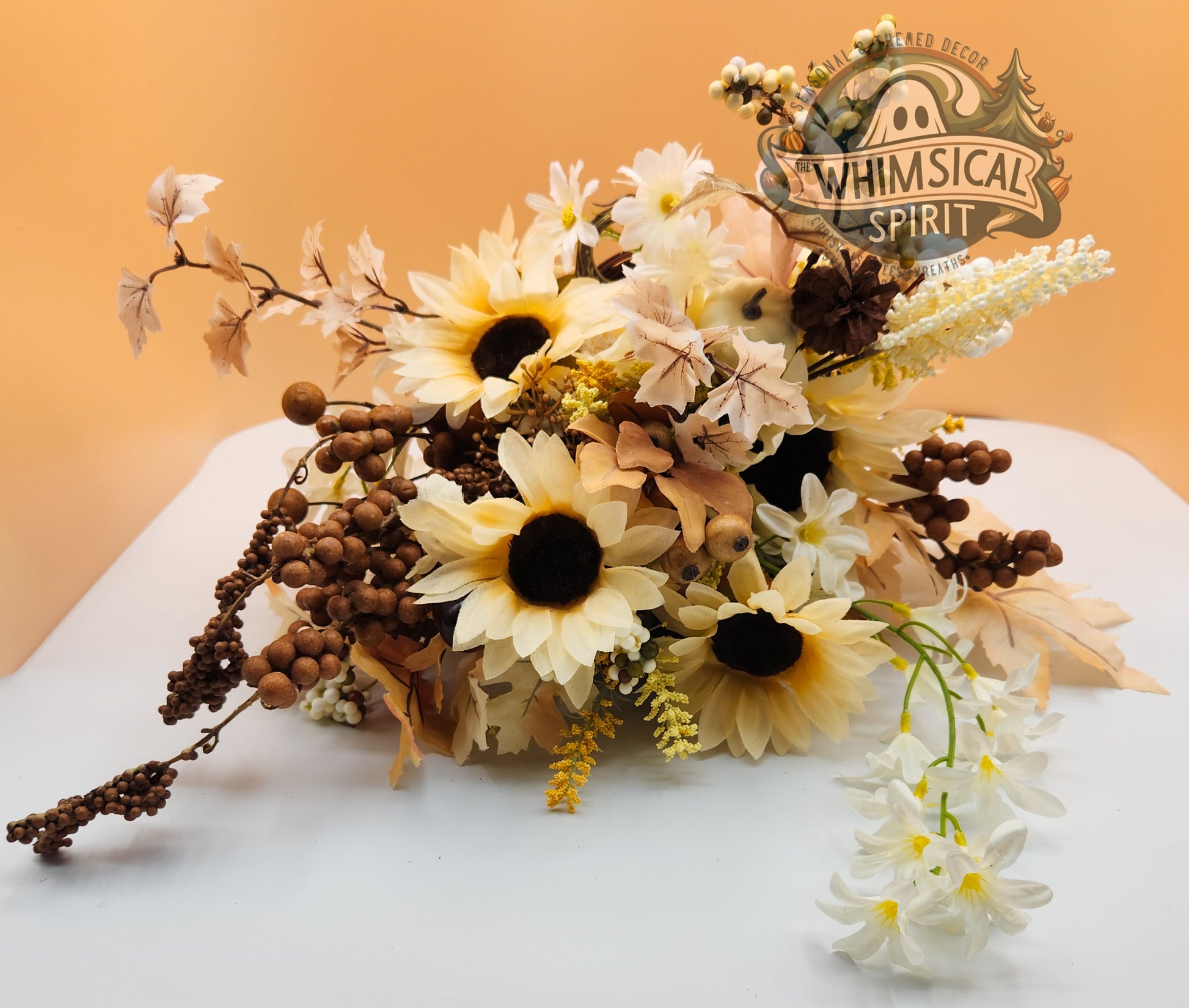 Sunflower and berry floral arrangement on a white surface, featuring greenery accents and Whimsical Spirit branded logo