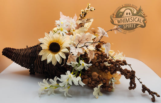 Decorative arrangement with flowers and a cornucopia on a white surface, branded 'Whimsical Spirit'.