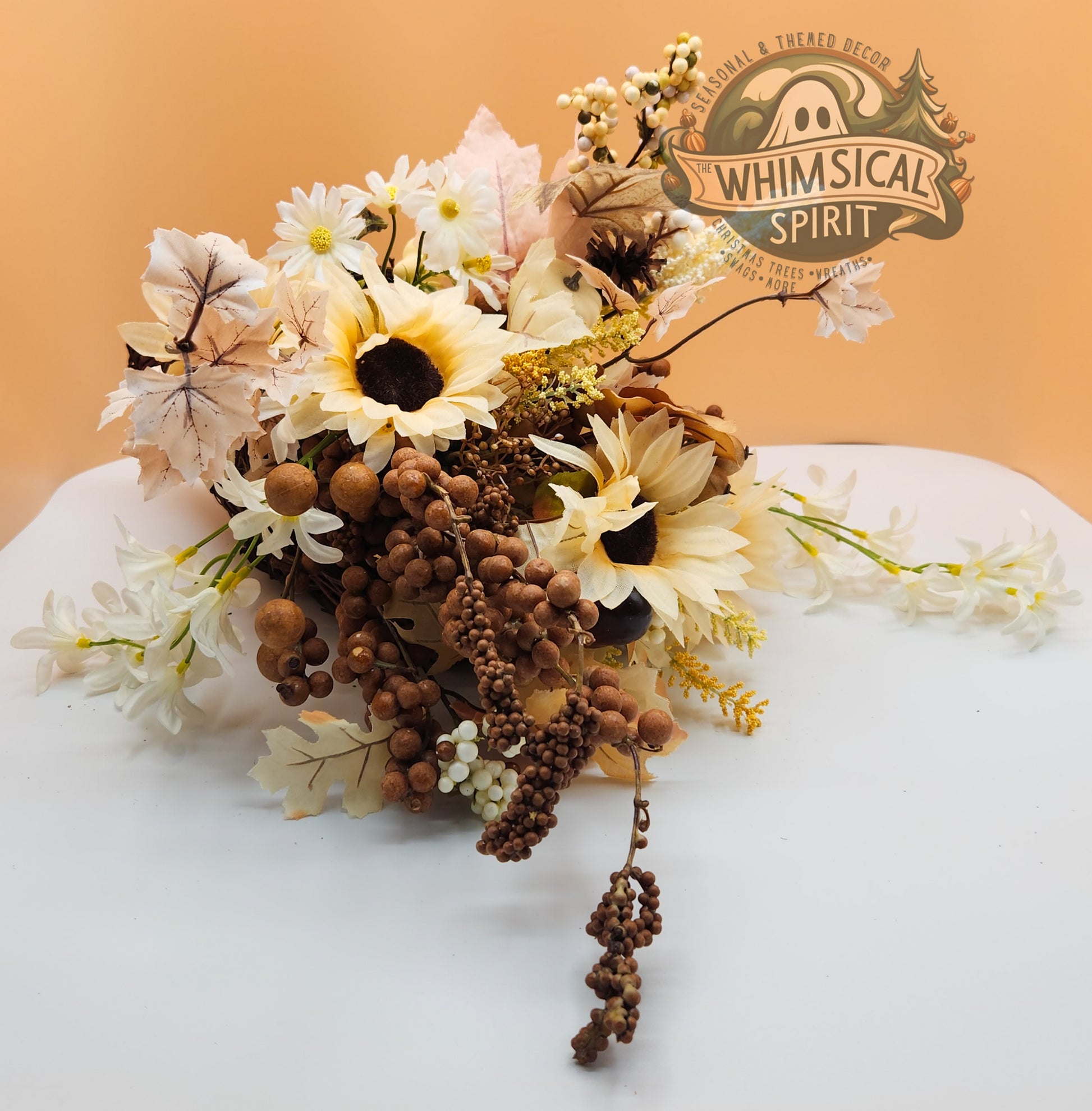 Seasonal floral arrangement with bright sunflowers, leaves, and berries on a white surface with  Whimsical Spirit logo