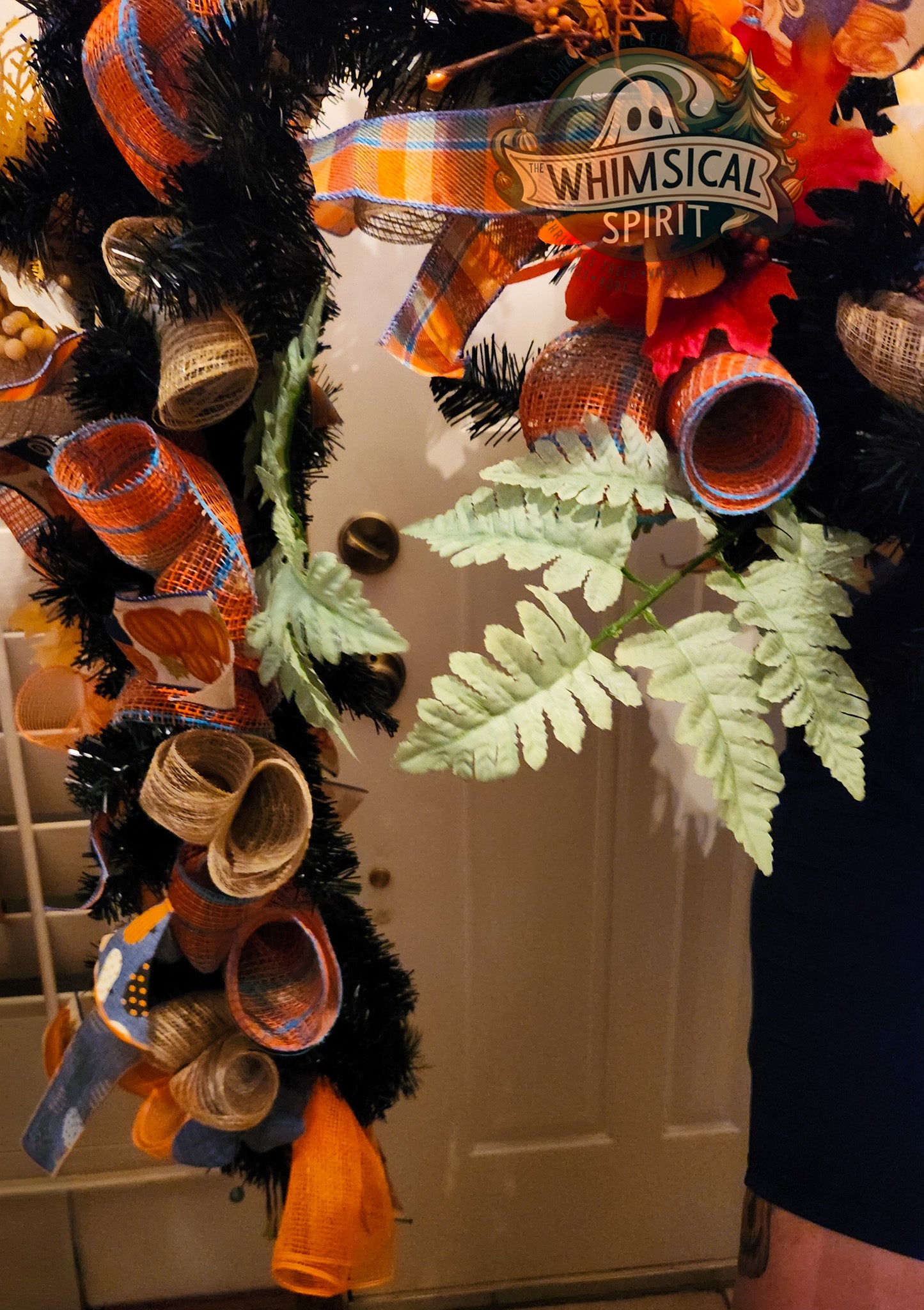 Decorative wreath with Fall-themed ribbons and leaves on a door.