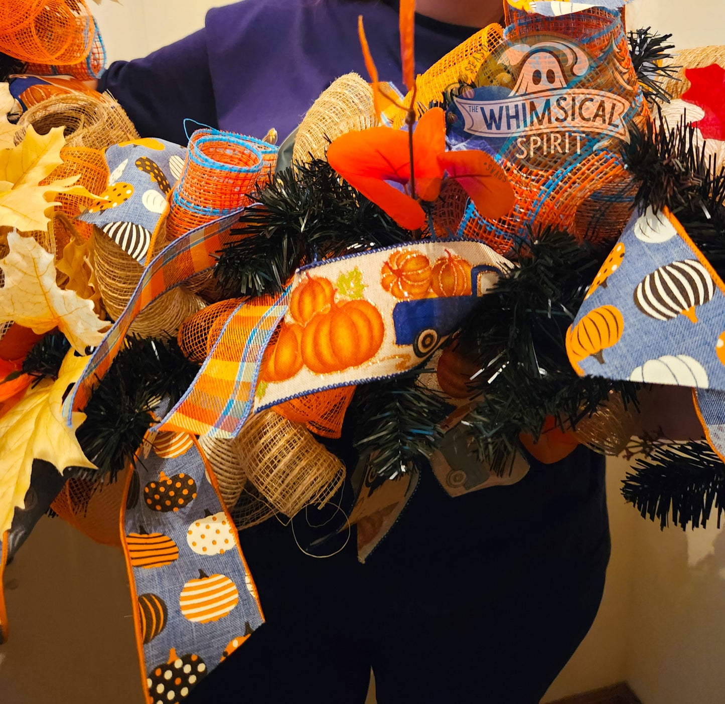 Fall-themed wreath with decorative ribbons and pumpkins on a plain background