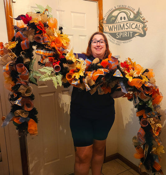 Person holding a large, colorful Halloween-themed wreath in front of a door with 'Whimsical Spirit' branding.