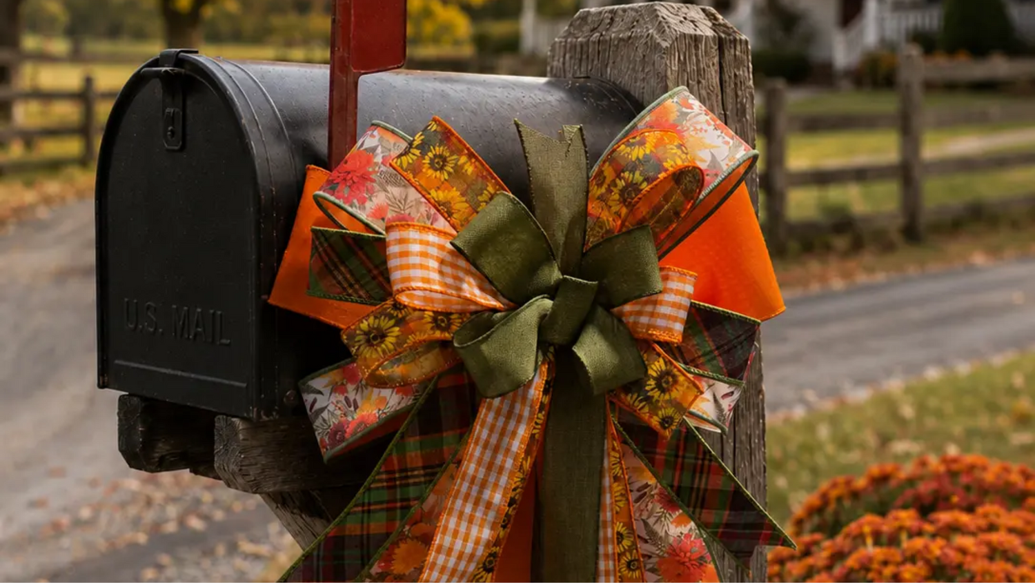 Handmade fall bow on a rustic mailbox with orange, green, plaid, gingham, and floral ribbon, styled with pumpkins and autumn mums.