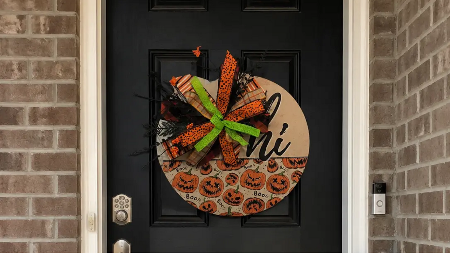 Handmade Halloween pumpkin door hanger on a black front door with orange ribbon, green bow, and playful spooky porch decor.