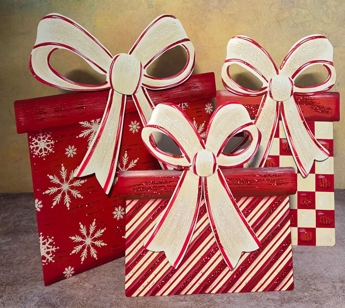 Front view of three coordinating Christmas present metal artworks featuring snowflake, diagonal stripe, and checkerboard patterns with oversized white bows.