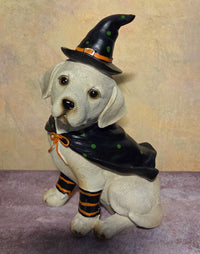 White Halloween dog figurine wearing a black witch hat, matching cape, and black-and-orange striped leg wraps.
