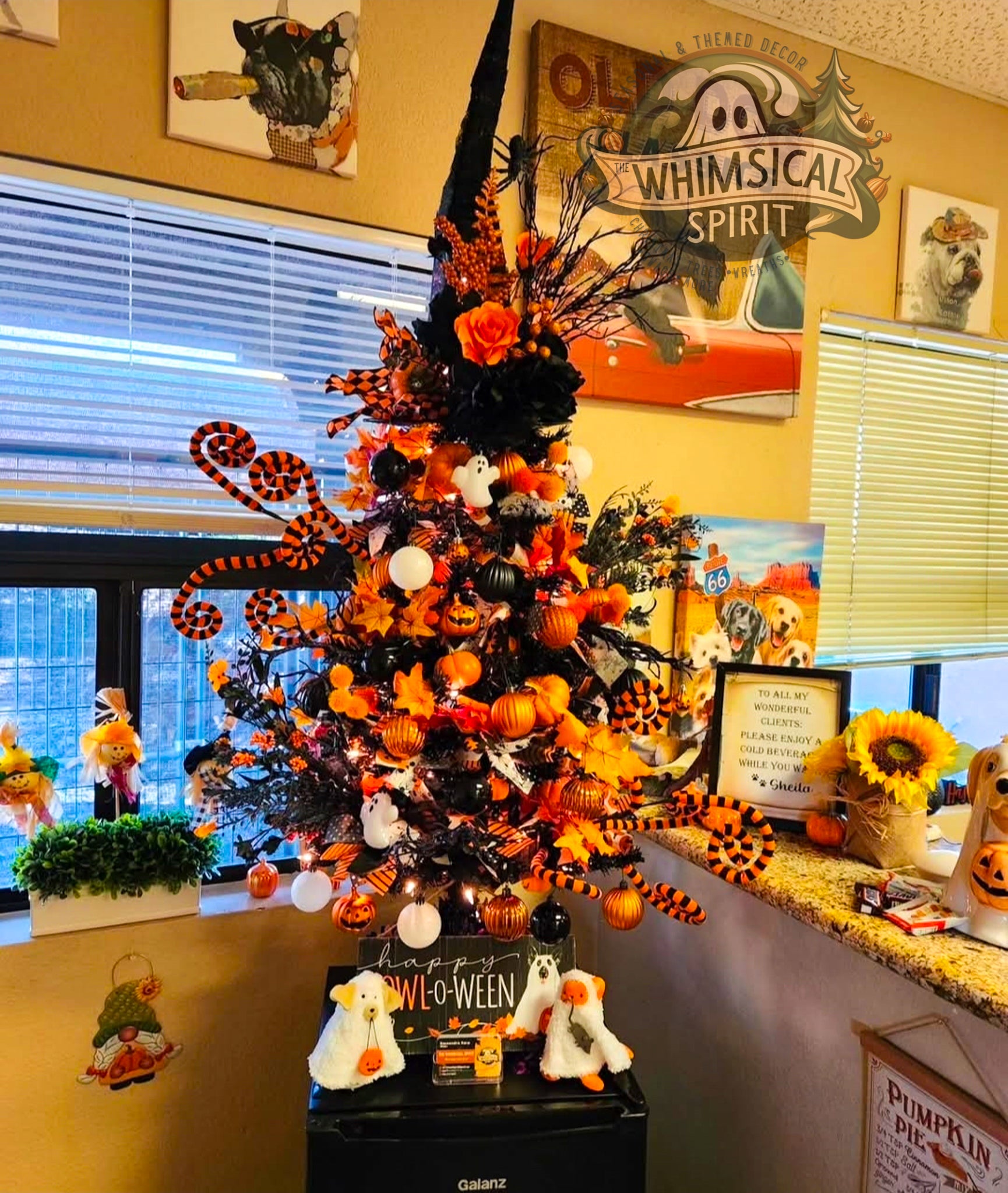Custom Halloween tree decorated with orange and black ornaments, ghosts, pumpkins, spooky ribbon sprays, and whimsical seasonal accents in a business setting.