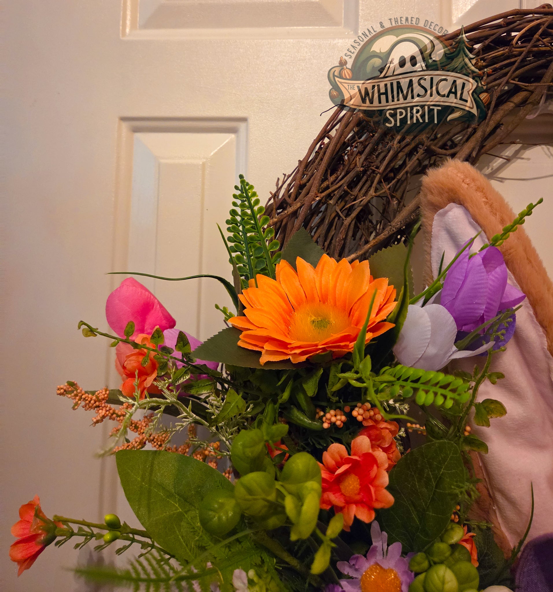 Colorful flower arrangement with a 'Whimsical Spirit' wreath in the background.