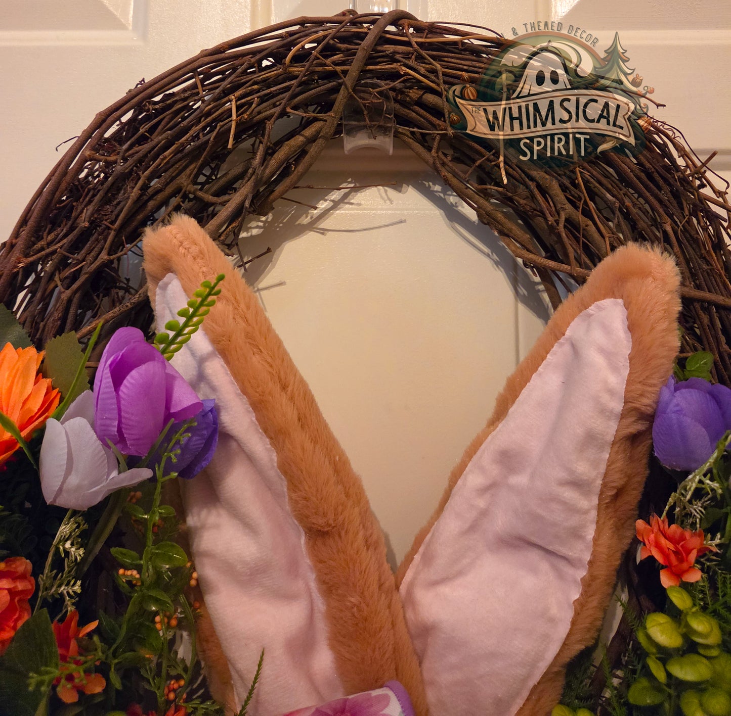Decorative wreath with bunny ears and flowers, branded 'Whimsical Spirit'.