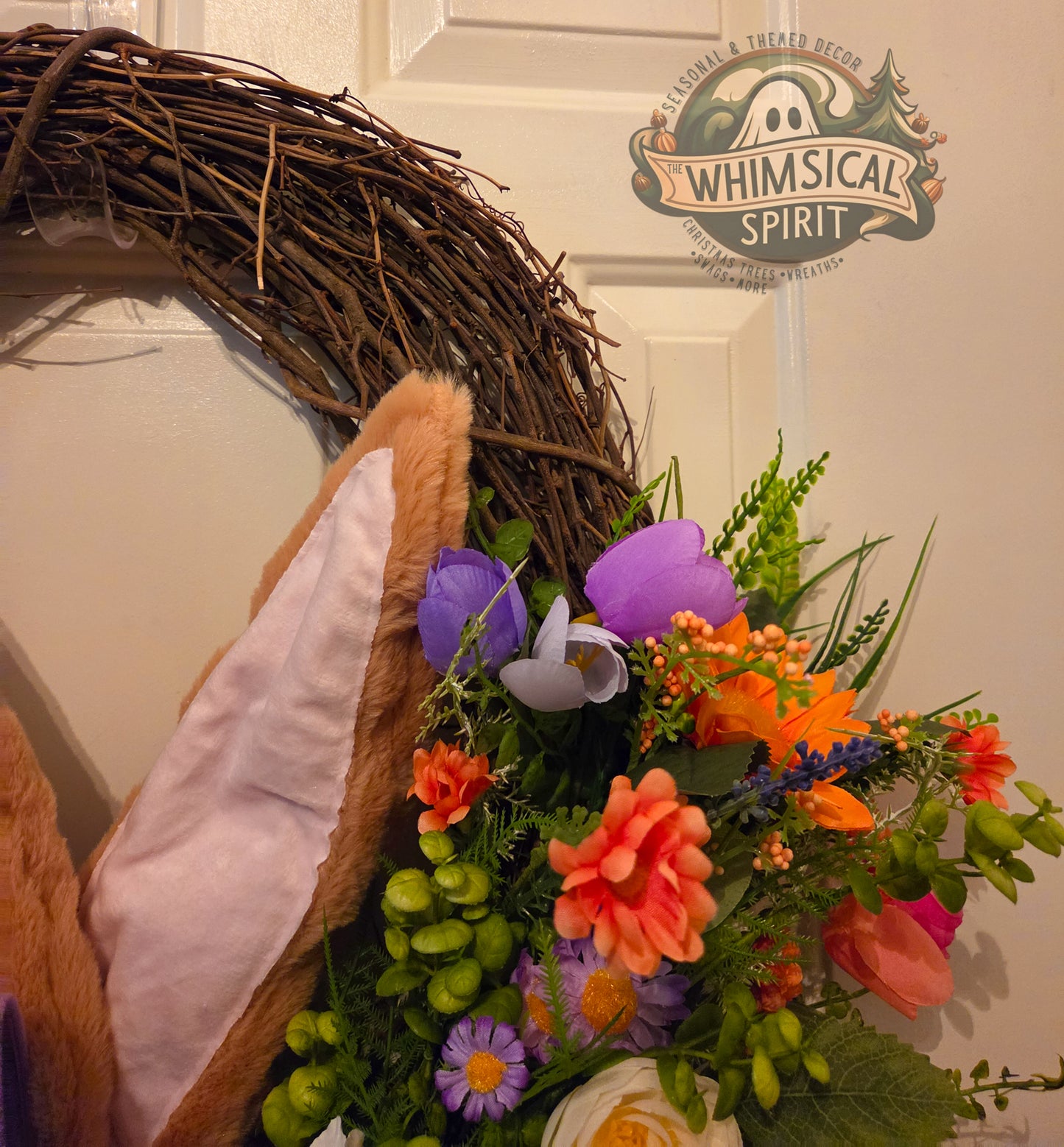 Decorative wreath with flowers and a teddy bear headband on a door, featuring 'Whimsical Spirit' branding.