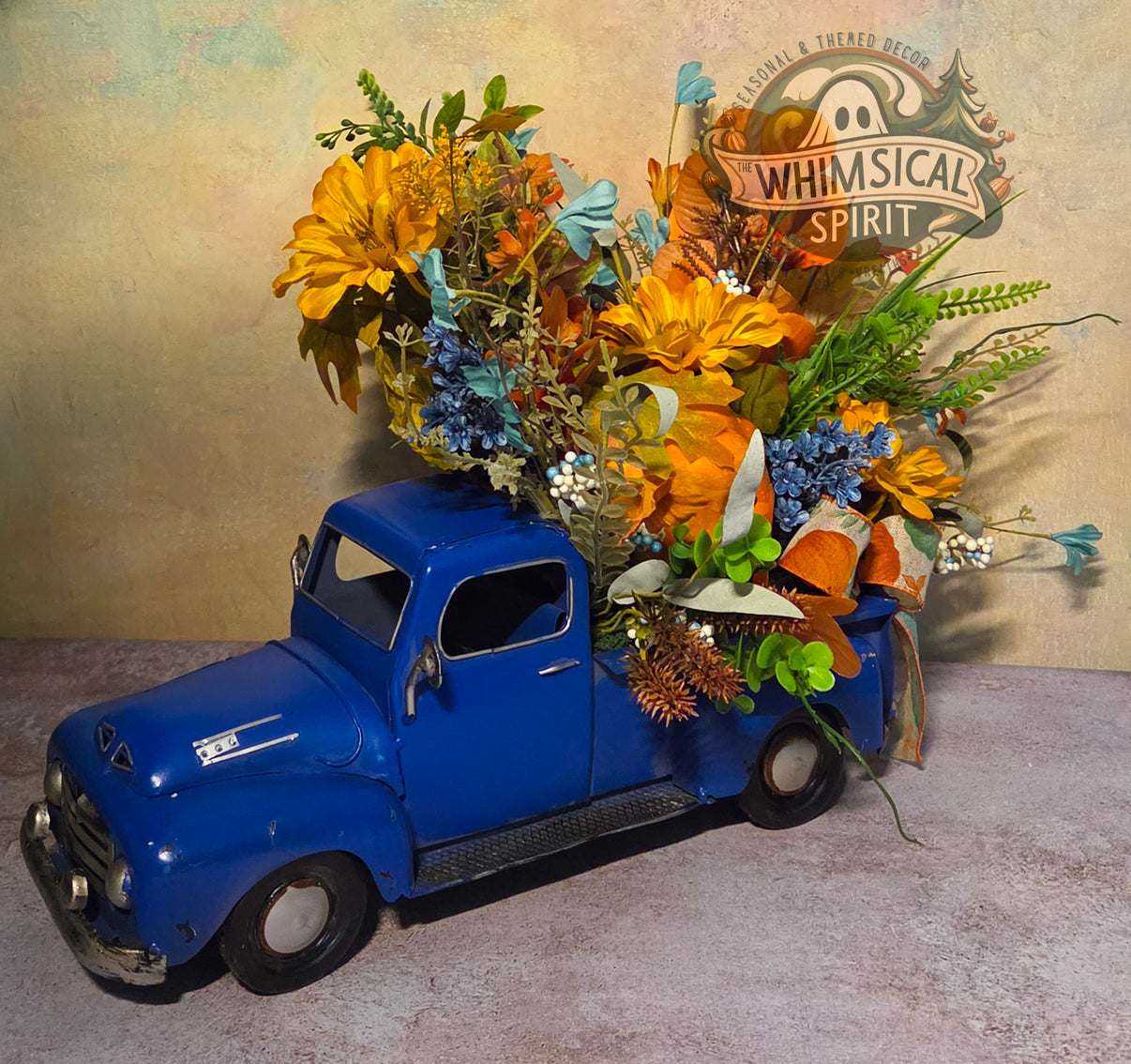 Handmade blue vintage truck fall centerpiece filled with pumpkins, golden flowers, blue blooms, berries, and greenery.