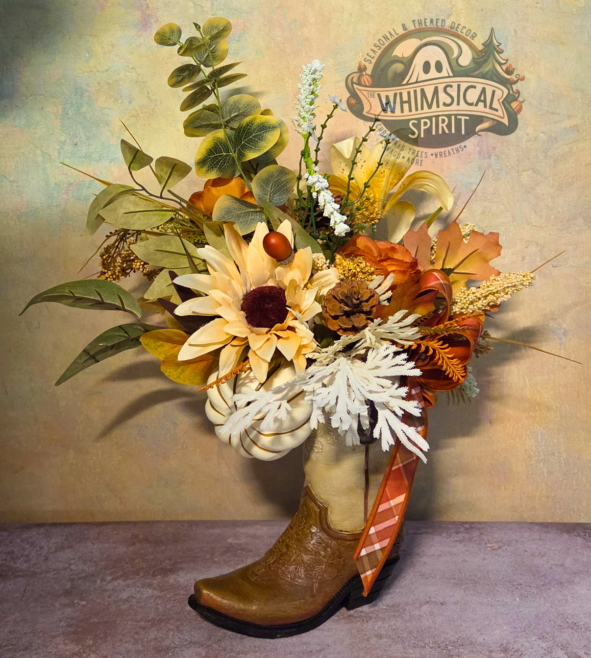 Handmade fall centerpiece in a brown cowboy boot with a cream sunflower, pumpkins, eucalyptus, pinecone, and plaid ribbon.