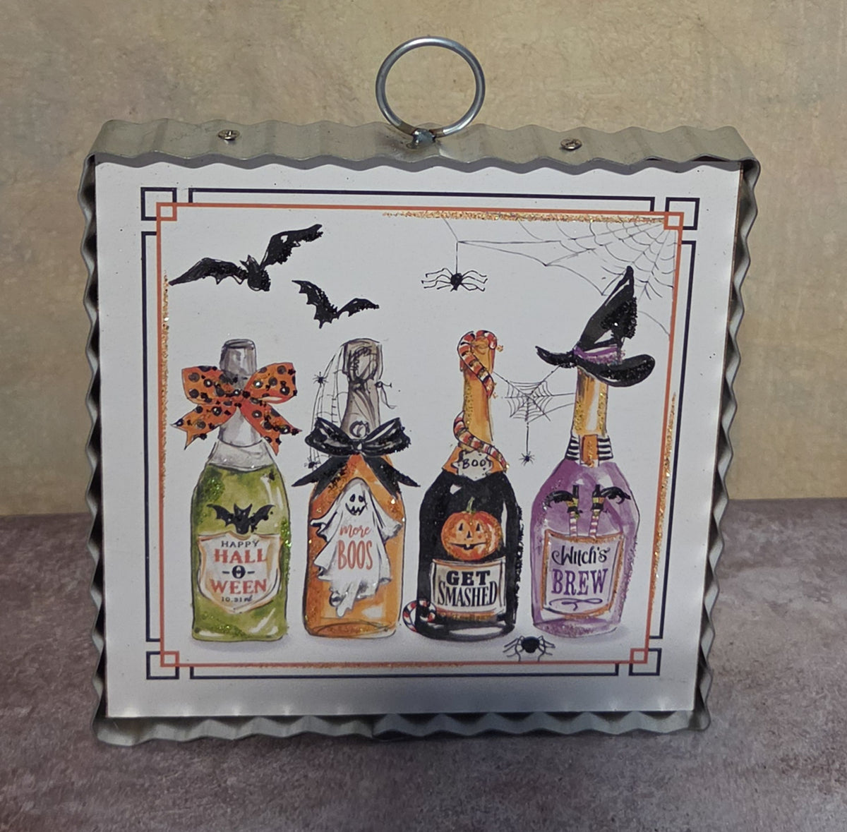 Bottled Boos framed Halloween metal art featuring four decorated potion bottles, flying bats, spiders, webs, and playful spooky labels.