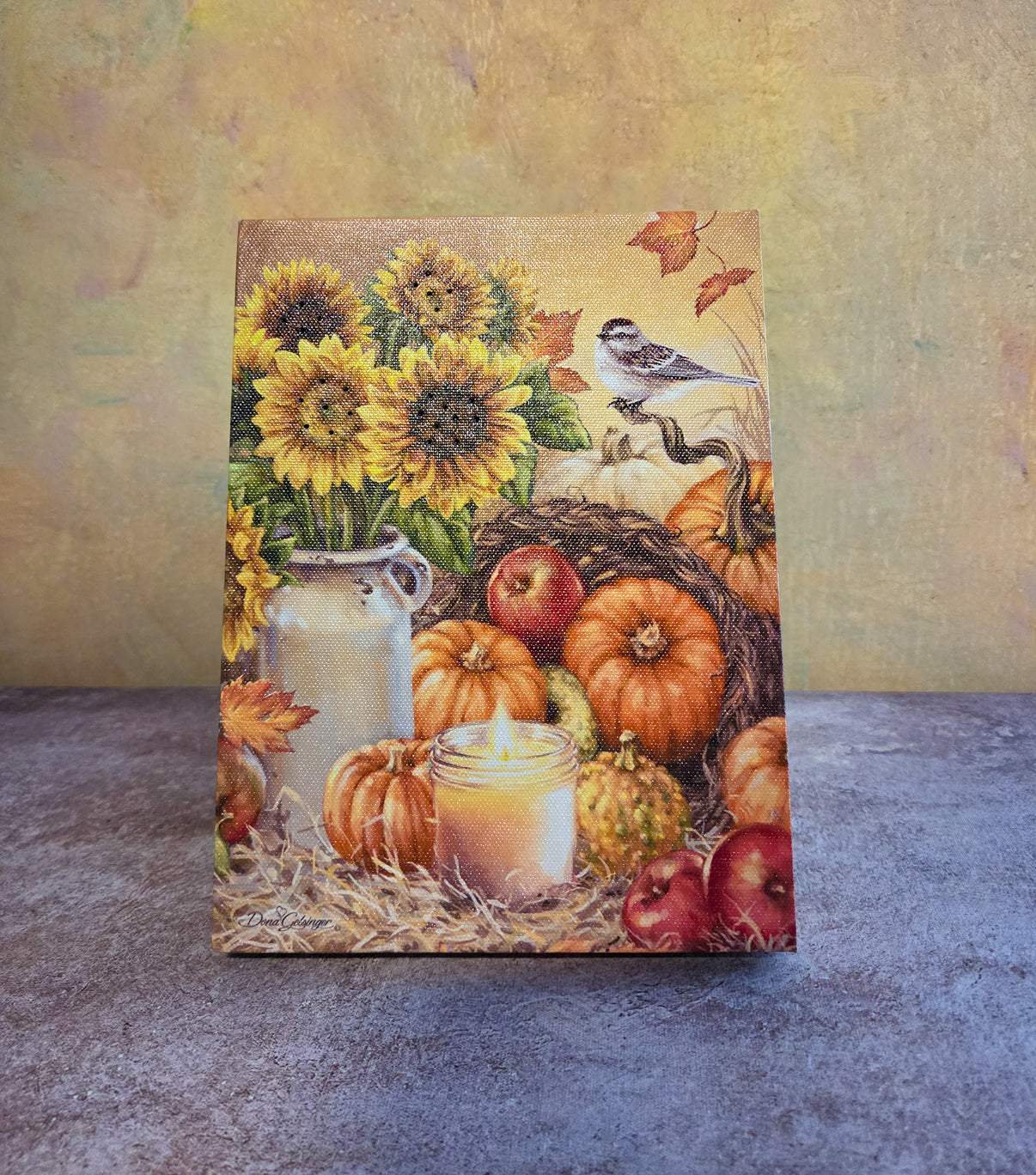 Bountiful Harvest light-up fall tabletop canvas featuring sunflowers, pumpkins, apples, glowing candle, fall leaves, and a small bird.