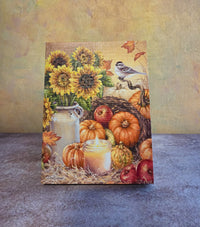 Bountiful Harvest light-up fall tabletop canvas featuring sunflowers, pumpkins, apples, glowing candle, fall leaves, and a small bird.