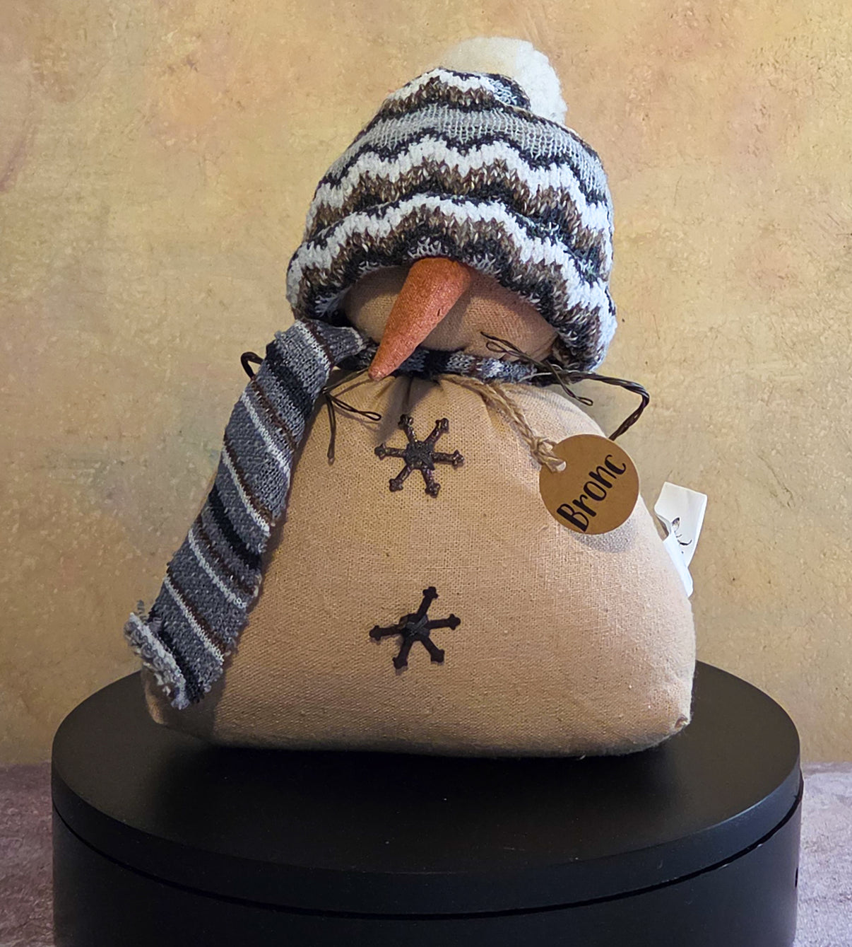 Bronc the Snowman winter soft sculpture shelf sitter with knit hat, striped scarf, carrot nose, stitched snowflake details, and name tag.