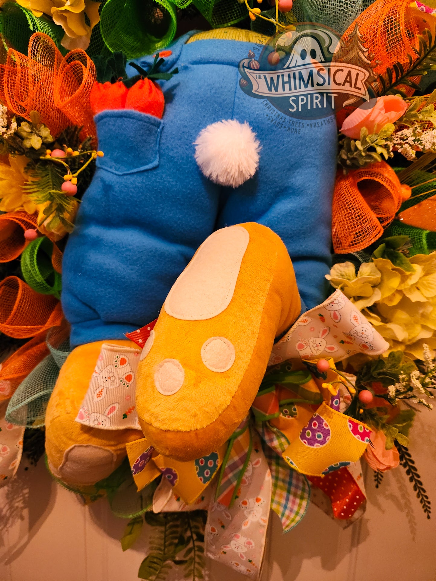 Decorative wreath with a blue and yellow character surrounded by flowers and ribbons.