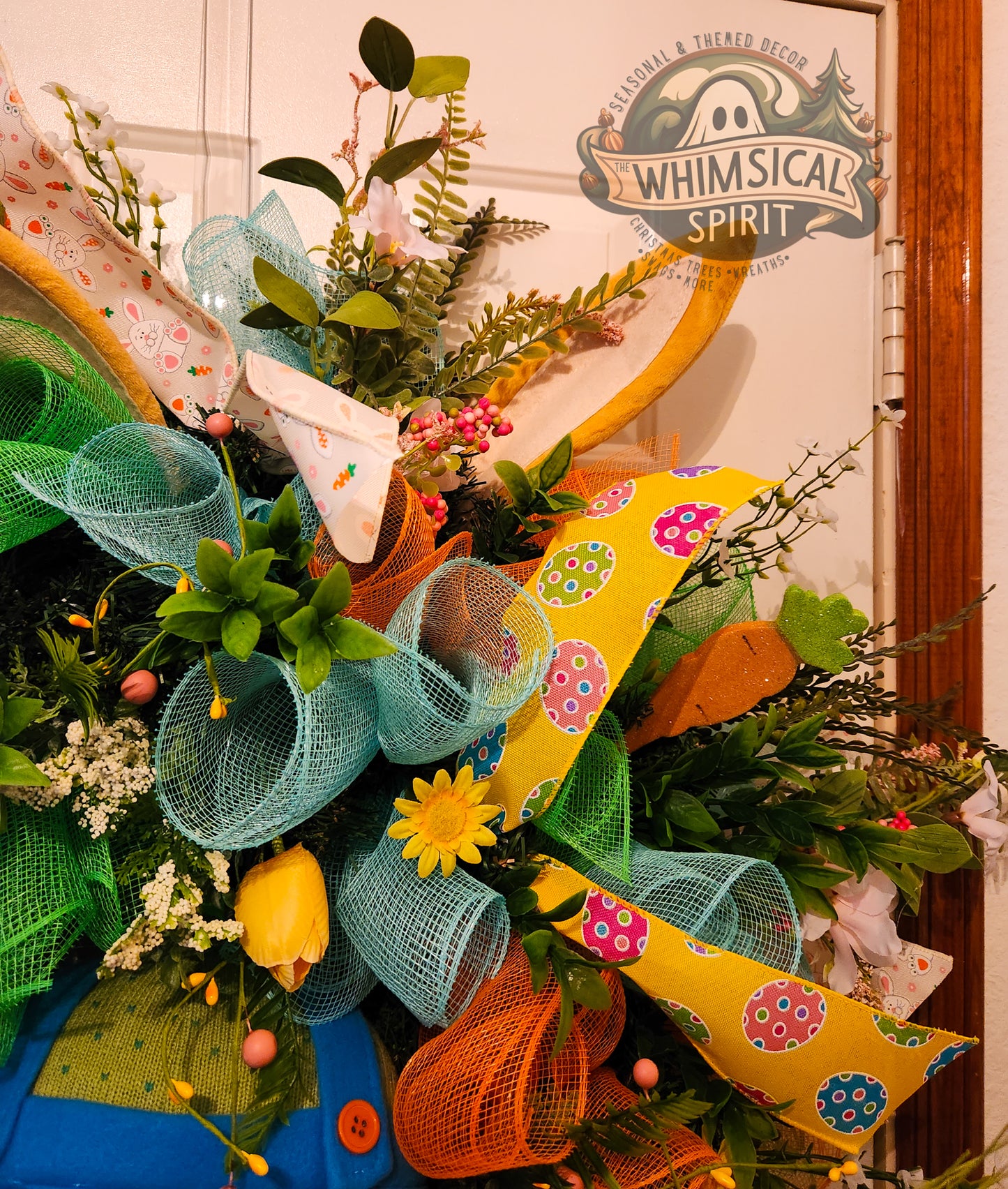 Colorful wreath with ribbons and flowers in front of a door with 'Whimsical Spirit' sign.