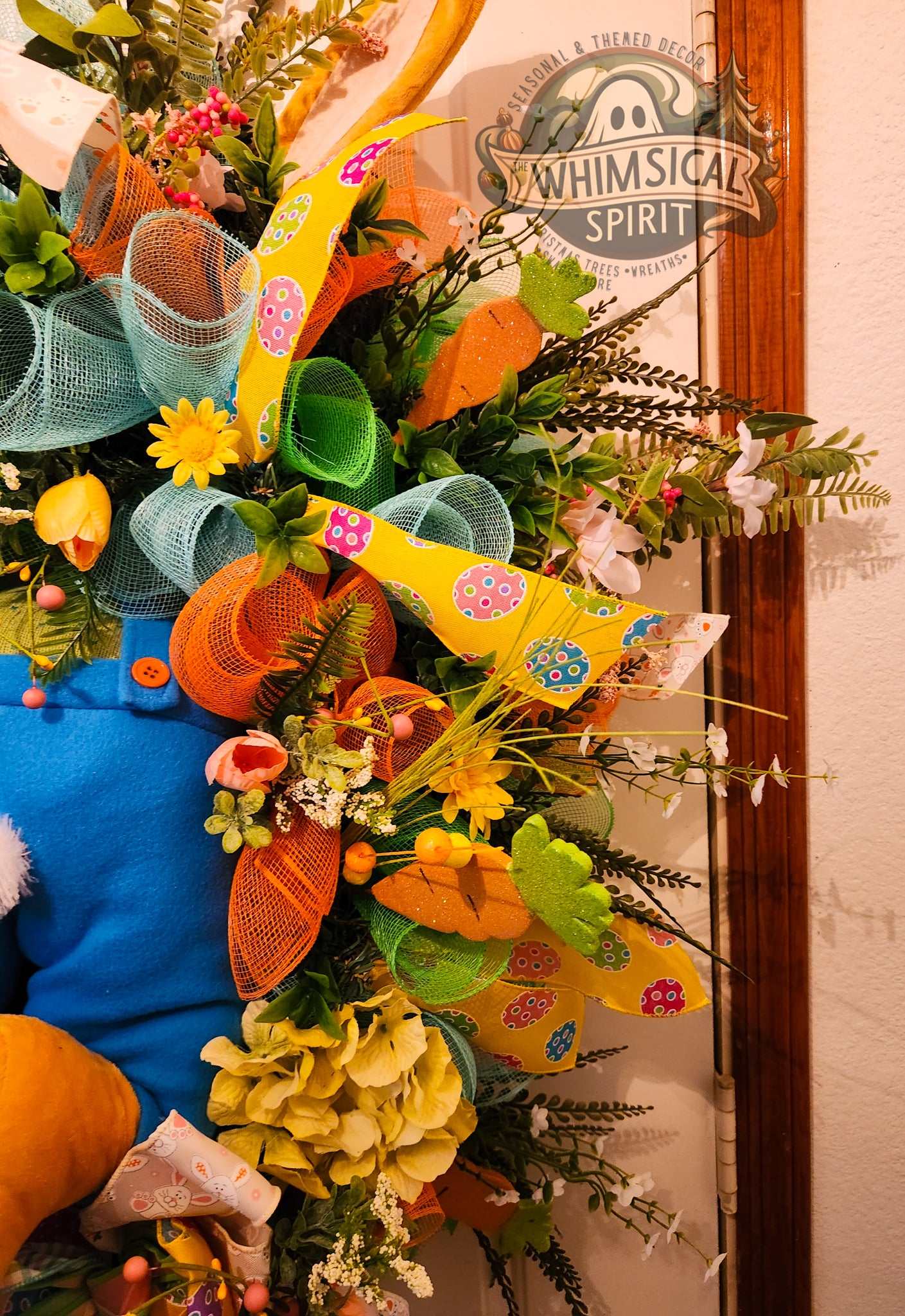 Decorative wreath with colorful ribbons and flowers in front of a store entrance.