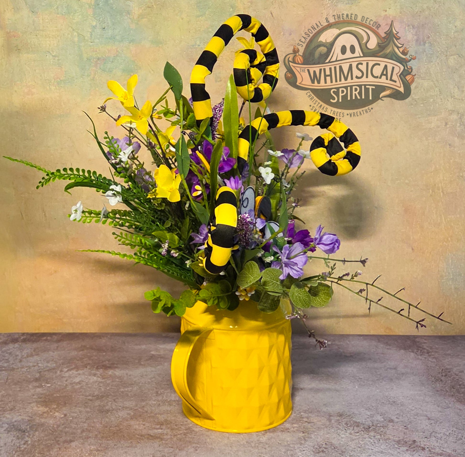 Floral arrangement with yellow and black striped elements in a yellow vase, branded 'Whimsical Spirit'.